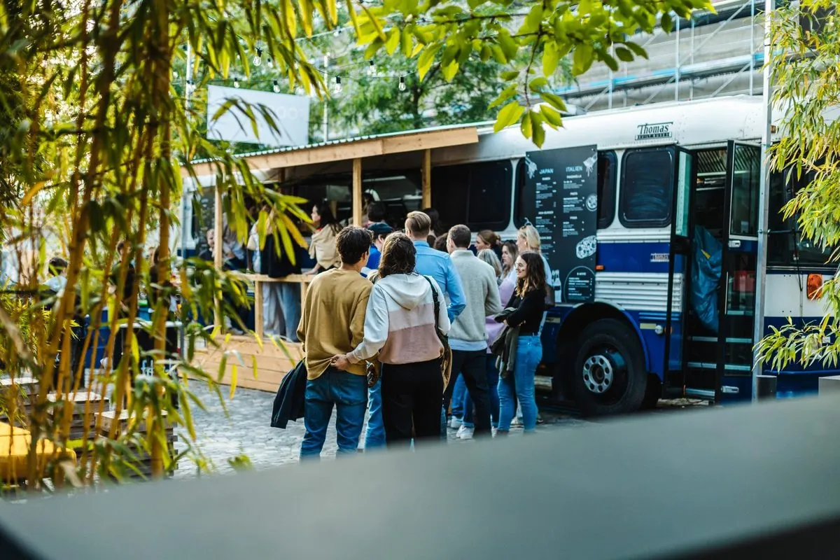 Gäste stehen am Abend vor dem weiß-blauen BAM!-Bus