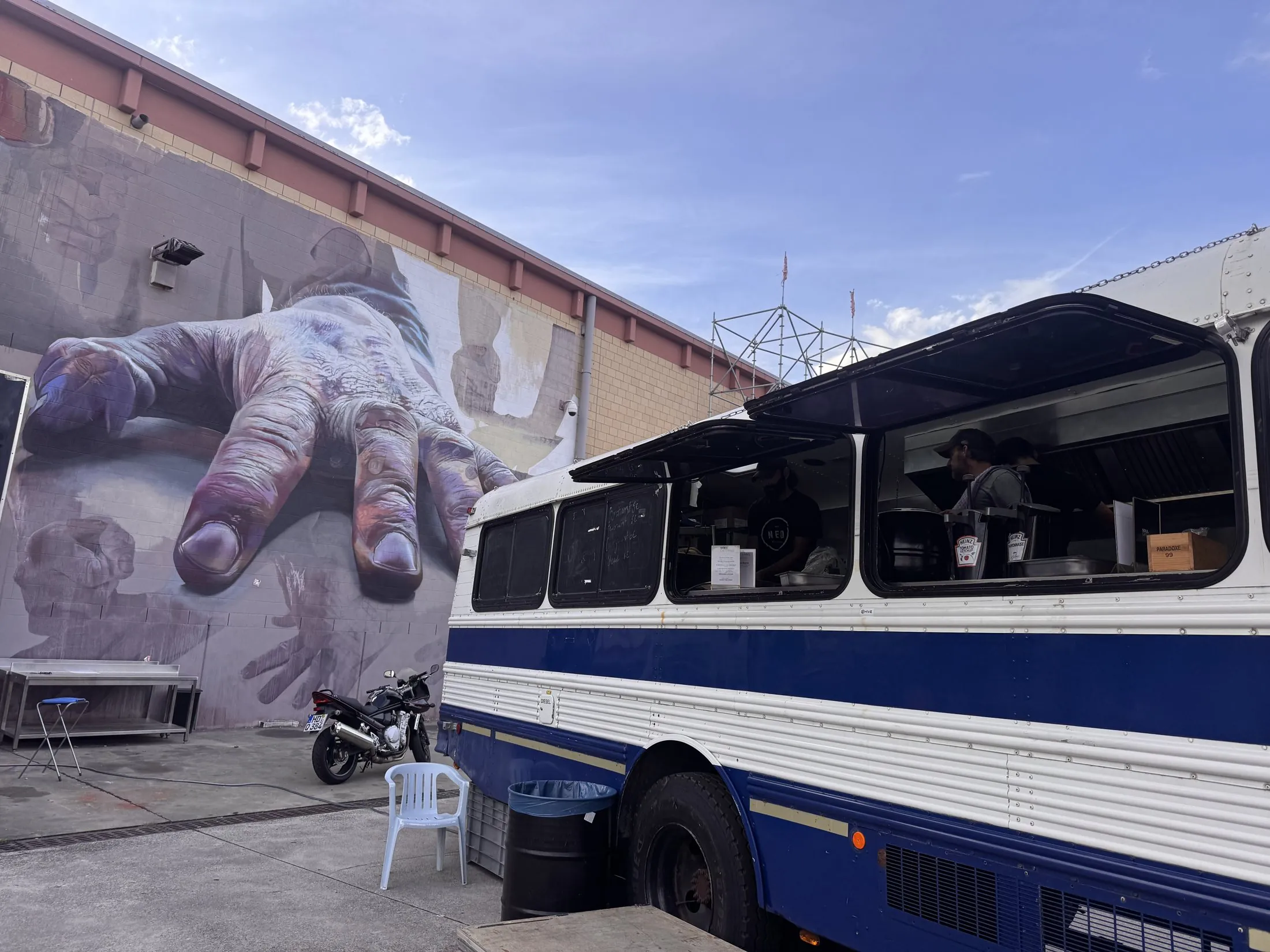 Der weiß-blaue BAM!-Bus mit offenen Fensterklappen vor einem großen Wandgemälde