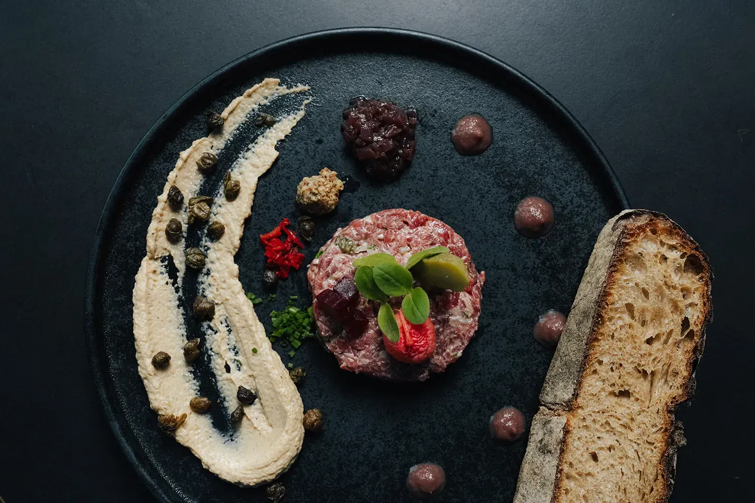 Rindertatar mit Kapern-Creme und Brot auf schwarzem Teller