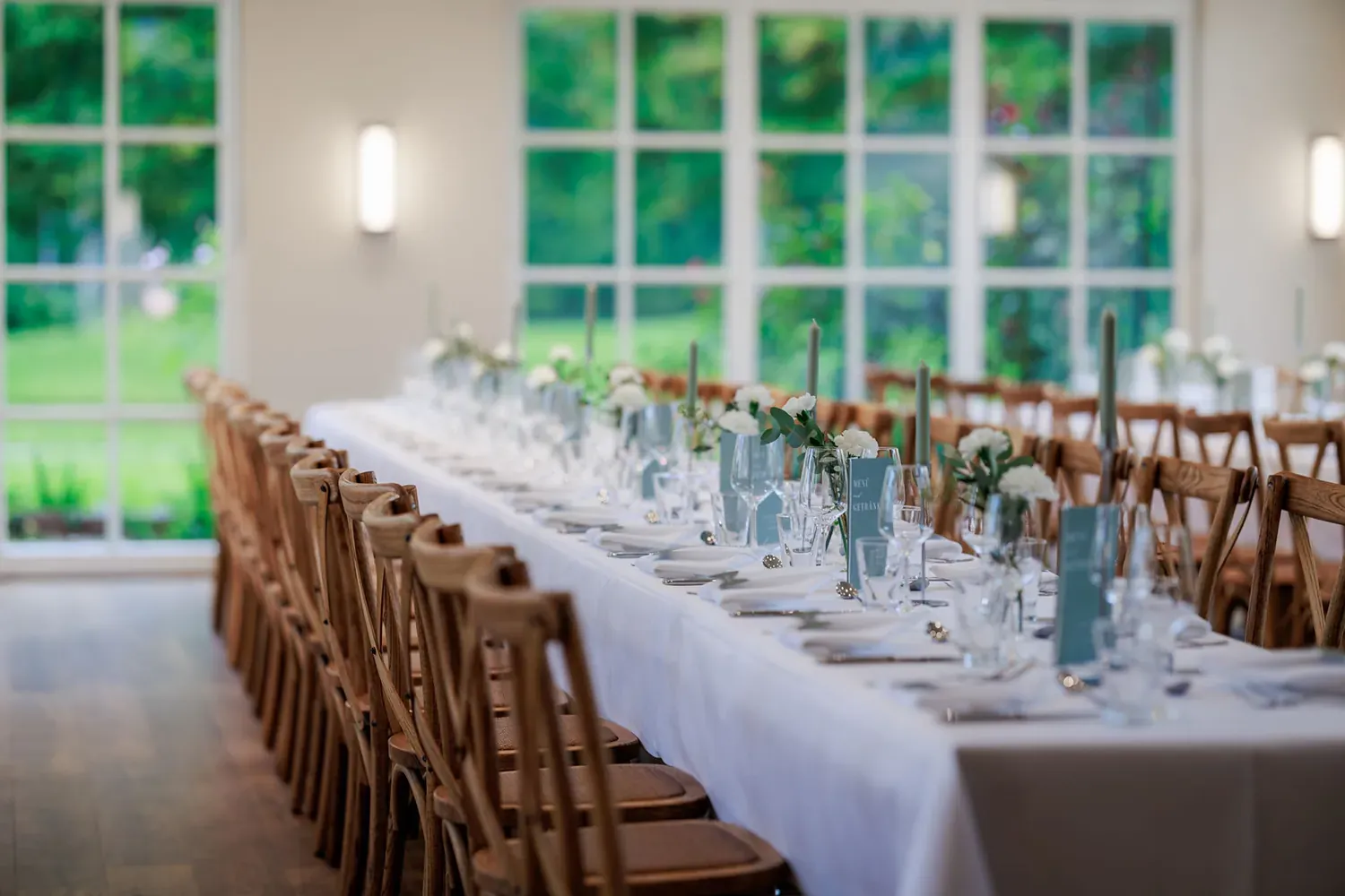 Lange weiß gedeckte Festtafel mit Nelken und Kerzen vor der Fensterfront der Orangerie